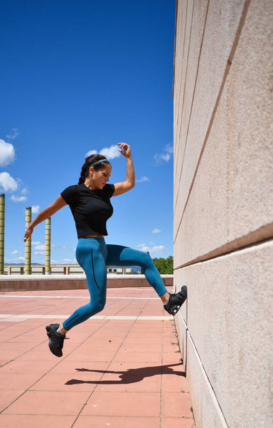 Fitness woman jumping hard towards a wall as a symbol of strength - Photo, Image