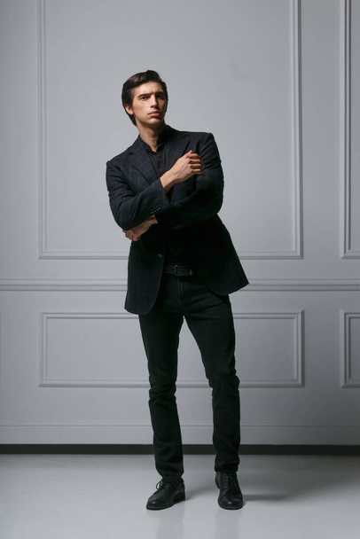 Imagen completa de un joven y elegante hombre de la moda ajustando su traje mientras mira a su lado, sobre fondo blanco
. - Foto, Imagen
