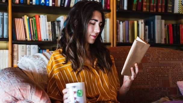 Молода жінка читає книгу з чашкою чаю на дивані
 - Фото, зображення