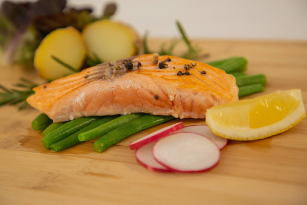 Filete de salmón fresco a la parrilla con judías verdes asadas, papas al horno, lima y verduras de ensalada es una dieta saludable para la dieta en un plato de madera
. - Foto, Imagen