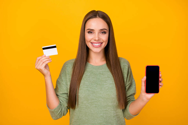 Portrait of positive cheerful girl hold smartphone credit card recommend buy new modern device pay with bank online system wear sweater isolated over bright shine color background - Φωτογραφία, εικόνα