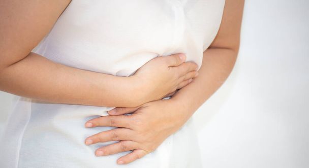 Образ жінки з Азії, яка тримає руку в животі через біль у шлунку, через біль у шлунку і інфекції, що передаються їжею на білому тлі.. - Фото, зображення