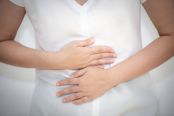 A imagem de uma mulher asiática segurando a mão em seu estômago por causa de uma dor de estômago, por causa de uma dor de estômago e ter infecções de origem alimentar em um fundo branco
. - Foto, Imagem