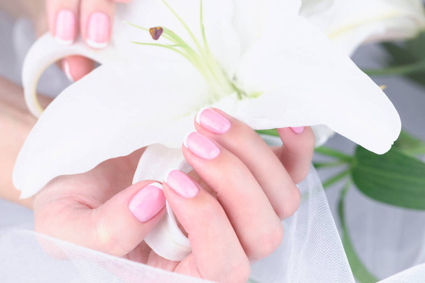 Manicure nuziale. Mano femminile con manicure francese con un giglio bianco su sfondo bianco
. - Foto, immagini