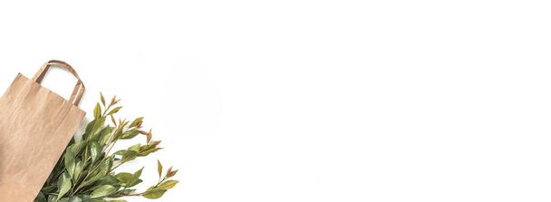 Переработанный коричневый пакет покупки бумаги с ручкой и зеленые ветви листья изолированы на белом фоне. Концепция нулевых отходов. Вид сверху, плоский, копировальное пространство. Баннер
. - Фото, изображение
