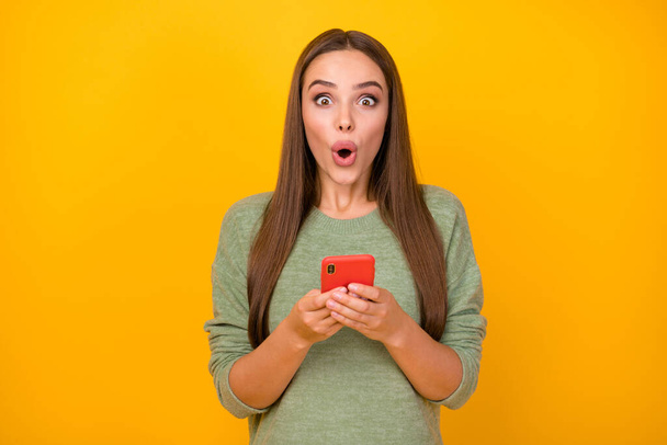 Portrait of astonished girl use smart phone impressed social network communication chatting friend answer scream wow omg wear sweater isolated over shine color background - 写真・画像