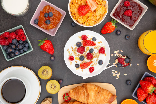 Breakfast Served in the morning with Butter croissant and corn flakes Whole grains and raisins with milk in cups and Strawberry, Blueberry, Raspberry, Kiwi, Fresh Orange Juice on the breakfast table. - Photo, Image
