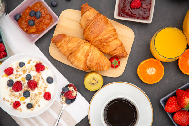 Café da manhã servido com café, croissant de manteiga e flocos de milho Grãos integrais e passas com leite em xícaras e morango, framboesa, Kiwi, suco de laranja fresco na mesa de café da manhã. - Foto, Imagem