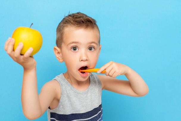 Diş fırçasıyla dişlerini fırçalayan ve diğer elinde bir elma tutan komik çocuk. - Fotoğraf, Görsel
