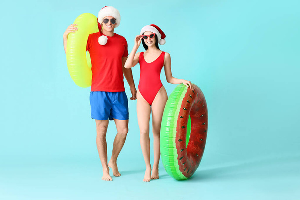 Giovane coppia con anelli gonfiabili e cappelli di Babbo Natale su sfondo colore
 - Foto, immagini