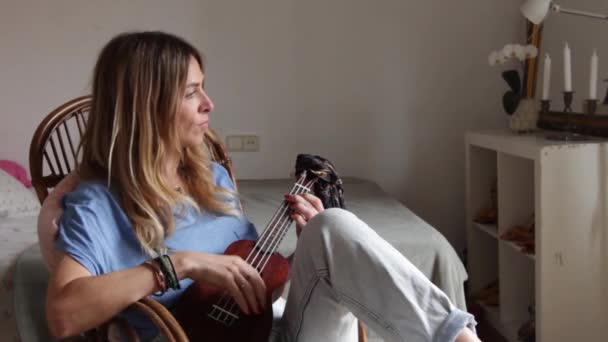 Woman at home sitting on an old chair play ukelele  - Materiaali, video