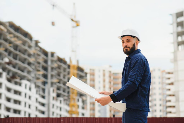 Engineer builder wearing safety vest with blueprint at construction site - Foto, Imagen