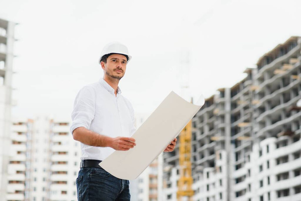 Engineer builder wearing safety vest with blueprint at construction site - Foto, imagen