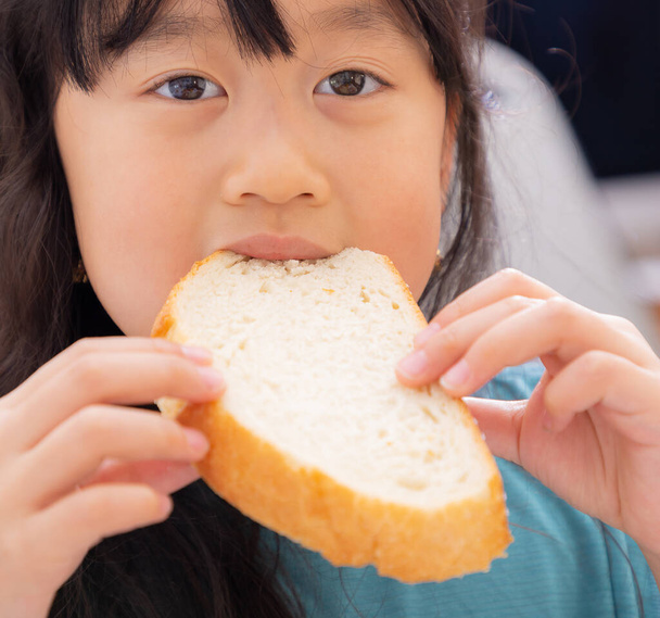A imagem de uma menina asiática com longos cabelos pretos comendo pão natural sem açúcar para a saúde e bom café da manhã para crianças todos os dias
. - Foto, Imagem
