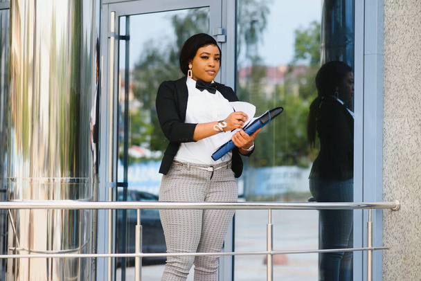 Conversation with the client. African businesswoman holding a cell phone in hand and talking on the phone with a client while standing near office. - Foto, Imagem