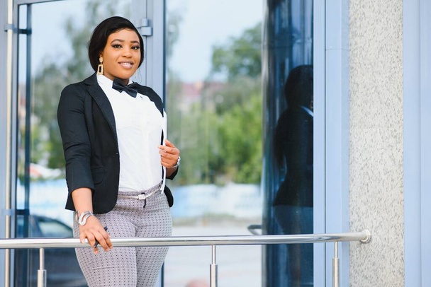 Pensive African American female lawyer in stylish formal suit holding folder with mock up area and looking away standing against courthouse. Half length of woman professional advocate with documents - Foto, Imagem