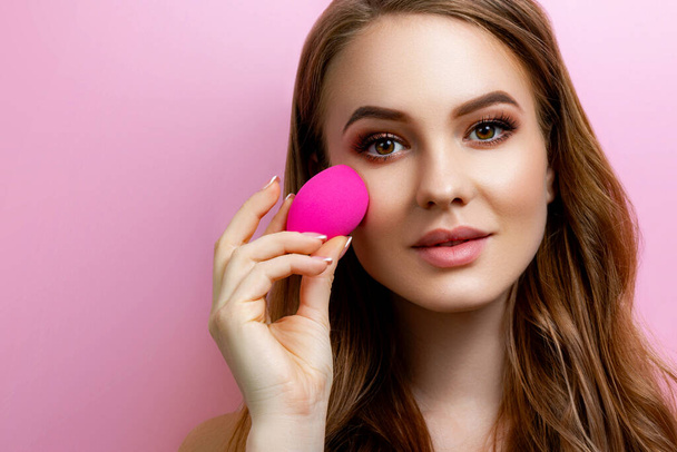 Girl with a makeup beauty blender on a pink background - Fotoğraf, Görsel