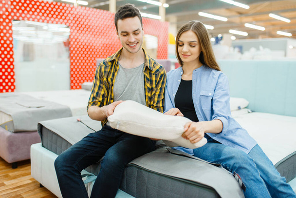 Young love couple choosing pillow in furniture store showroom. Man and woman looking samples for bedroom in shop, husband and wife buys goods for modern home interior - 写真・画像