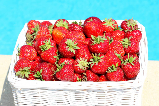 Fresas frescas maduras en una canasta blanca de mimbre después de recoger bayas rojas dulces sobre un fondo de agua azul
. - Foto, imagen