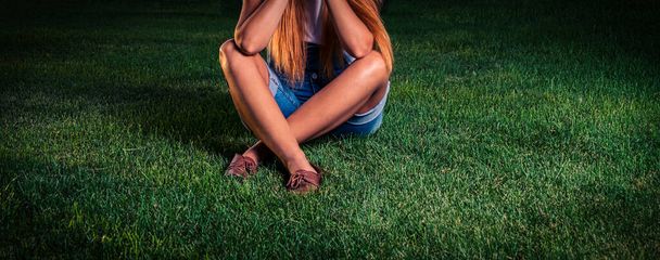 Teenage girl is sitting on the park grass cross-legged and preparing for exams - Photo, Image