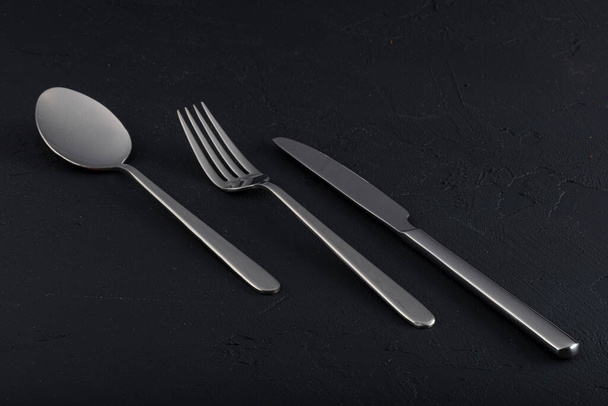 Assiette vide, fourchette, couteau, cuillère, couverts isolés sur fond bois noir, vue de dessus. - Photo, image