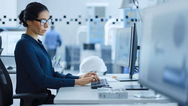 Beautiful Female Engineer Working on Personal Computer in the High-Tech Industrial Factory, She Uses CAD Software to Model Heavy Industry High Tech Mechanism 3D Model. Side View Shot - 写真・画像