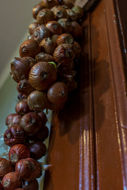 Μικρά κόκκινα κρεμμύδια δεμένα σε κλωστή, κρεμασμένα στον τοίχο - Φωτογραφία, εικόνα