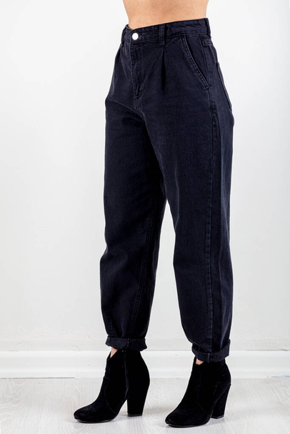 Studioaufnahmen Herbst-Winter-Konzept. Eine Frau steht auf, trägt schwarze Jeans (Hose, Jeans) und schwarze Lederstiefel für isoliertes Weiß im Studio. - Foto, Bild