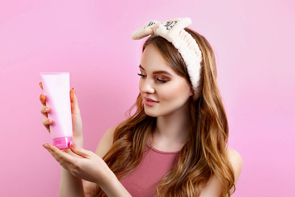 Studio portrait of a cute girl with a tube of cream on a pink background - Fotografie, Obrázek