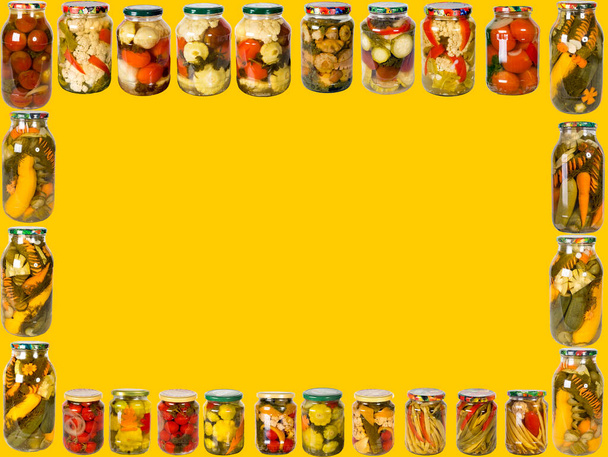 Marco de una variedad de frascos de vidrio con verduras enlatadas sobre un fondo amarillo. Conservas de verduras caseras
. - Foto, Imagen