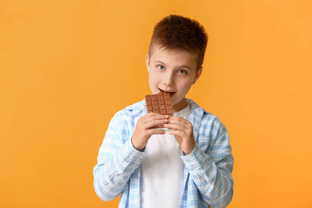 Cute little boy eating chocolate on color background - Photo, Image
