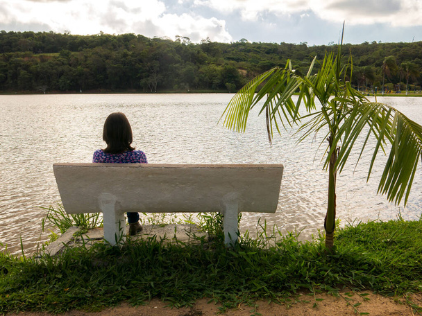 Nierozpoznana dziewczyna siedzi w fotelu przed jeziorem w podświetleniu - Zdjęcie, obraz
