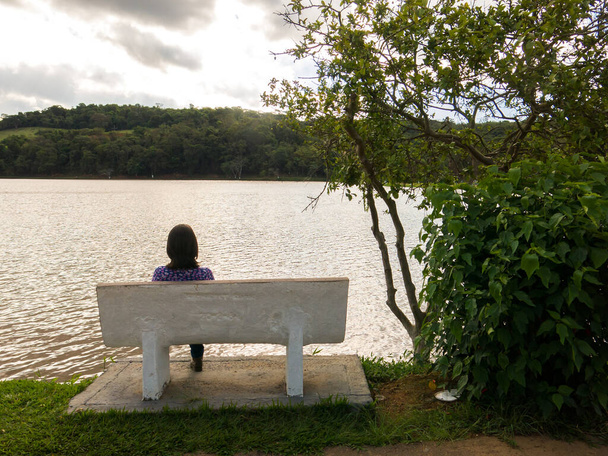 バックライトの湖の前の席に座っている認識されていない女の子 - 写真・画像