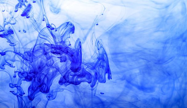 Blue ink injected into water from syringe, colour mixing with water creating abstract shapes. - Фото, зображення