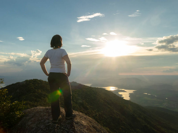 Nierozpoznane osoby - dziewczyna na szczycie górskiego szczytu, krajobraz i zbiornik zaporowy - podświetlenie zachodu słońca - Zdjęcie, obraz