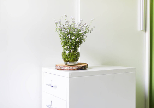 Μπουκέτο από το όμορφο γαλάζιο της άνοιξης και λευκά λουλούδια forget-me-not στο φως φόντο. Φυτό μυοσίτιδας. Φυσική διακόσμηση. Floral σύνθεση σε ξύλινη φέτα σε μινιμαλιστικό ανοιχτό εσωτερικό - Φωτογραφία, εικόνα