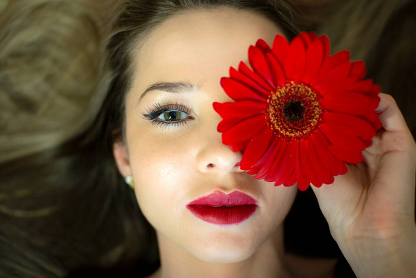 Πορτρέτο ενός κοριτσιού με ένα κόκκινο λουλούδι gerbera. - Φωτογραφία, εικόνα