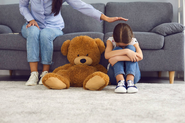 Aufgebrachtes kleines Mädchen weint auf dem Boden neben Teddybär, während Mutter sie zu Hause tröstet. Eltern beruhigen ihr unglückliches Kind - Foto, Bild