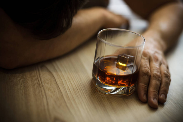 Cierra las manos de un hombre deprimido, durmiendo en la mesa, con un vaso de whisky en la mano. Concepto de pobreza, alcoholismo y depresión
 - Foto, Imagen