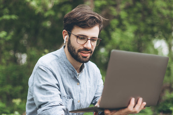 jóképű szakállas férfi szemüvegben szabadúszóként egy laptopon dolgozik a hegyekben. Szabadúszó koncepció - Fotó, kép