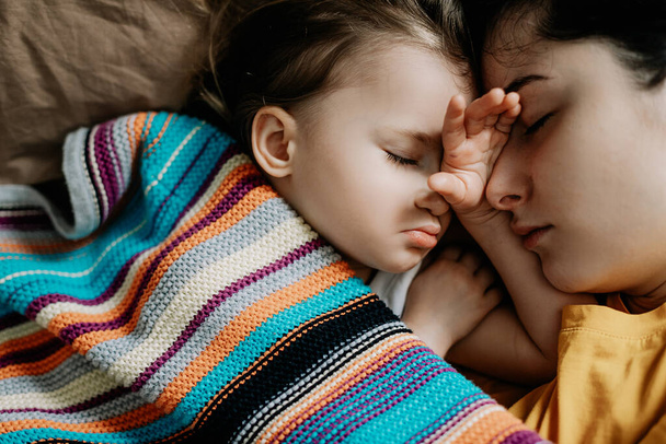Vue du dessus d'une belle jeune mère et de son mignon petit bébé dormant au lit à la maison - Photo, image