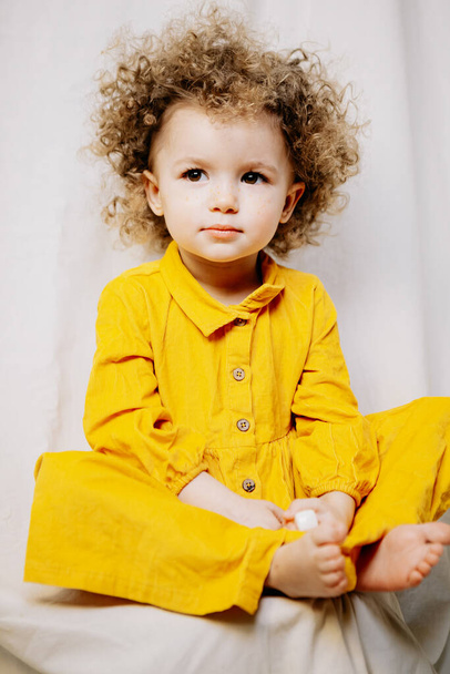 Portrait of attractive cute baby dressed in yellow dress posing on light background in home improvised photo studio - Zdjęcie, obraz