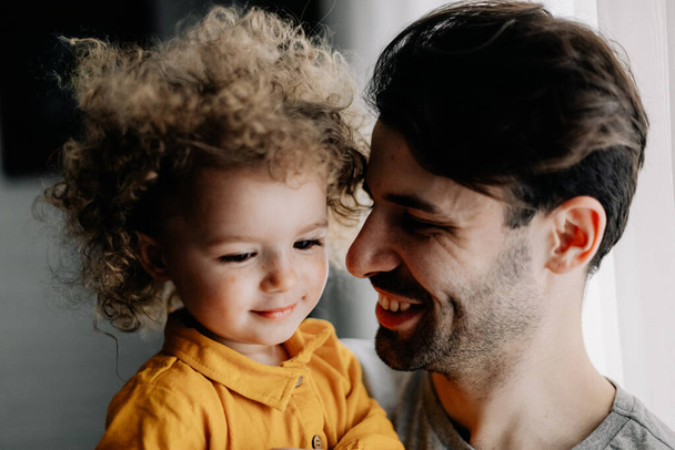 father and daughter. Young pretty dad and his little curly daughter hugging and having fun at home - Fotoğraf, Görsel