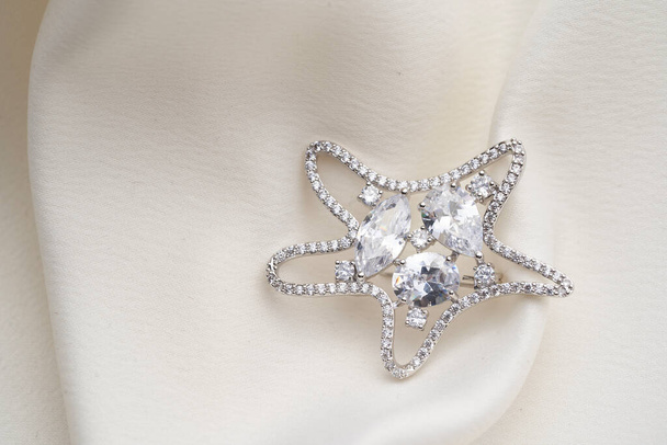 Серебряная брошь в форме морской звезды, с маленькими бриллиантами и красивыми кристаллами, изолированными на белом фоне
.  - Фото, изображение