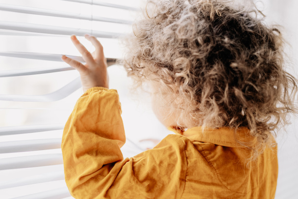 Curly baby looks out the window with bright sunlight. Copy space - Photo, Image