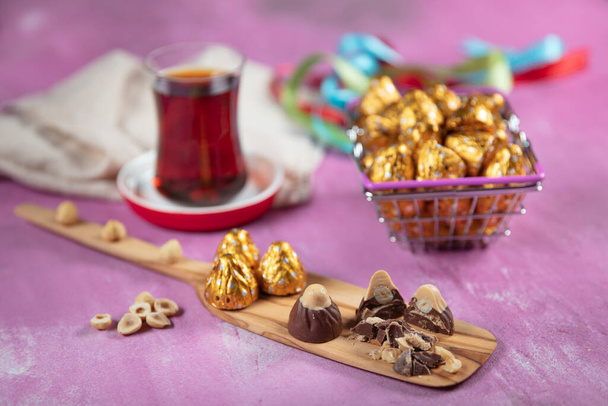Chocolate de avelã; Chocolate de avelã é enrolado em folha de ouro, no fundo de madeira lila. Conceito de Eid al-Fitr (Festa do Ramadã)
. - Foto, Imagem