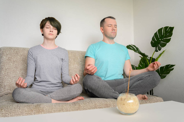 Father and daughter are meditating, sitting in lotus position on the couch. Yoga at home. - Foto, Imagem