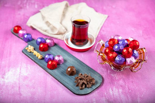 ヘーゼルナッツチョコレート;木製のリラの背景に赤、紫とピンクの箔で覆われたヘーゼルナッツチョコレート。イード・アル=フィトル(ラマダーン月の饗宴)の概念. - 写真・画像