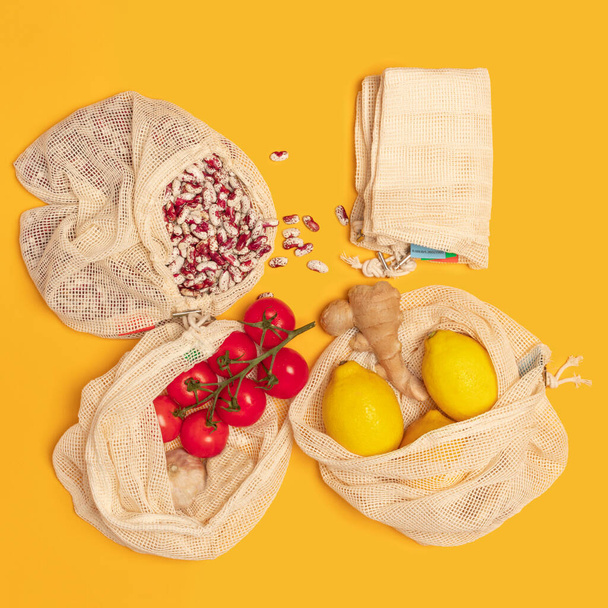 Víceúčelová sada bavlněných a síťovaných eko tašek pro nakupování. Nulový odpad, bezplastový koncept. Udržitelný životní styl. cherry rajčata, citróny, zázvor, červené fazole na žlutém pozadí. přírodní materiál. - Fotografie, Obrázek