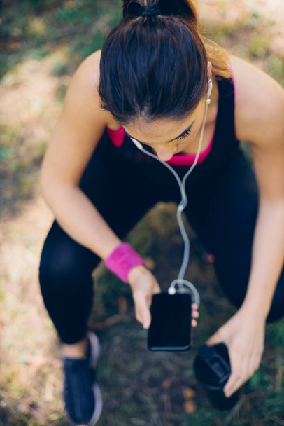 Vista aérea da mulher esportiva em forma agachado, usando telefone e se preparando para correr em um belo dia ensolarado
. - Foto, Imagem
